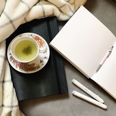 a cup of green tea next to an open notebook and two pens on a blanket