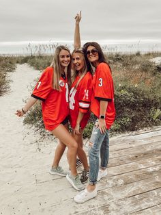 three girls in red jerseys are posing on the beach