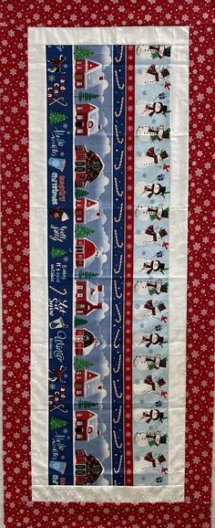 a red white and blue quilted wall hanging with christmas scenes on the front, along with santa's sleighs in the background