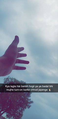 a person's hand reaching up into the sky with trees in the background and clouds overhead