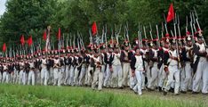 a large group of men in uniform marching down a road with red and white flags