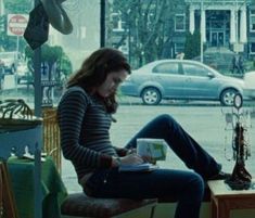 a woman sitting on top of a chair in front of a window holding a book