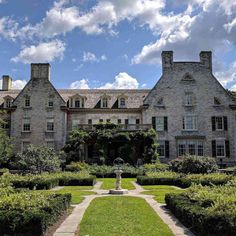 an old stone house surrounded by hedges and bushes with a fountain in the front yard