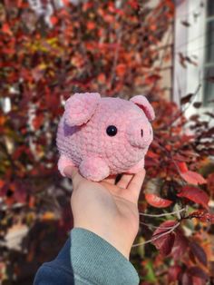 a hand holding a pink stuffed animal in front of some trees with red leaves on it