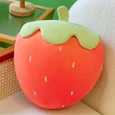 a strawberry shaped pillow sitting on top of a white couch next to a green table