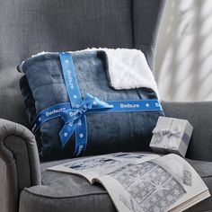 a gray chair with a blue and white blanket on top of it next to an open magazine