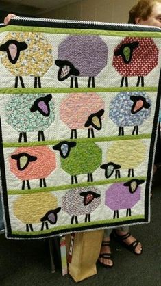 a woman holding up a quilt with sheep on it