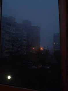 the view from inside a window at night with buildings and street lights in the distance