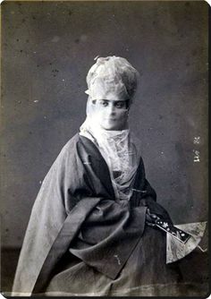 an old black and white photo of a woman with short hair, wearing a cape