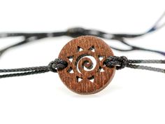 a wooden bracelet with black string and an intricate design on the front, sitting on a white surface