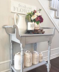 a table with jars and vases on it in front of a stair case that reads fresh cut flowers