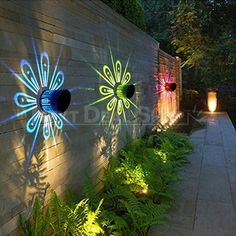 some lights that are on the side of a wall and in front of plants, bushes and trees