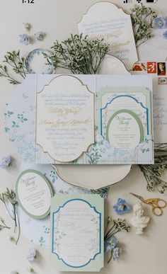 the wedding stationery is laid out on top of each other, with blue flowers and greenery