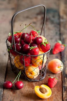 a metal basket filled with fruit on top of a wooden table next to peaches and strawberries