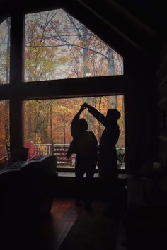 two people standing in front of a window with the sun shining on them and trees outside