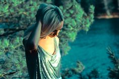 a woman with blonde hair wearing a silver dress and standing in front of some trees