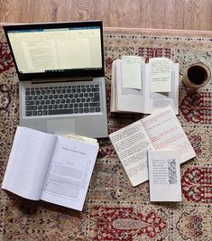 an open laptop computer sitting on top of a rug covered in books and papers next to a cup of coffee