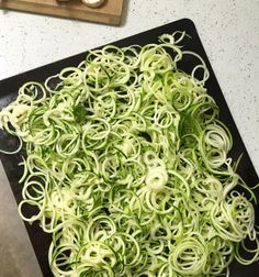 a black cutting board topped with lots of zucchini noodles and broccoli florets