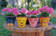 four potted plants with faces painted on them sitting on a table in the garden