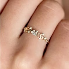 a woman's hand wearing a gold ring with flowers and leaves on the band