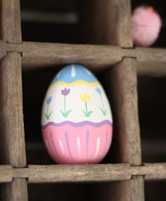 a painted egg sitting on top of a wooden shelf next to a pink pom - pom