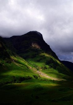 the mountains are covered in green grass under a cloudy sky with dark clouds above them