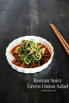 a white bowl filled with green onion salad next to chopsticks on a table