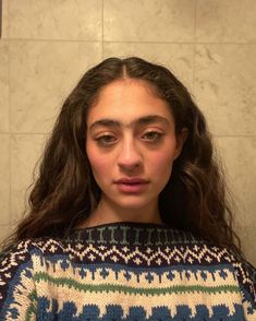 a woman with long hair standing in front of a tiled wall and looking at the camera