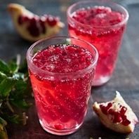 two glasses filled with red liquid sitting on top of a wooden table next to leaves