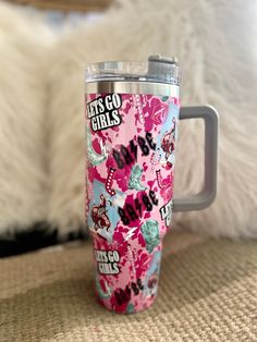 a pink and blue travel mug sitting on top of a couch next to a white furnishing