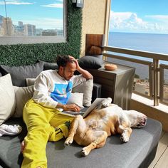 a man sitting on top of a couch next to a brown dog laying on it's side