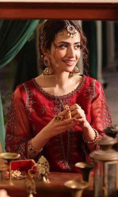 a woman in a red dress is smiling and looking at her jewelry on the table