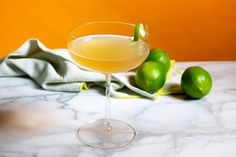 a drink in a coupe glass with limes on the side and a towel next to it