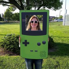 a woman holding up a green video game controller costume for her face to the camera