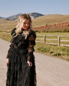 a woman in a black dress is walking down the road