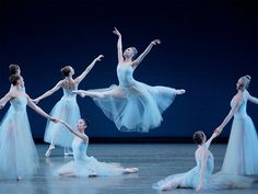 four ballerinas in blue tutus and white dresses, one is holding her leg up