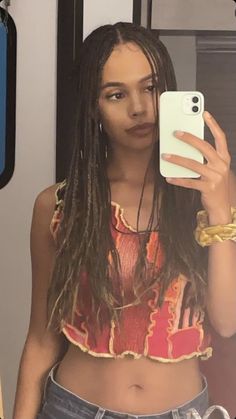 a woman with dreadlocks taking a selfie in the mirror while holding her cell phone