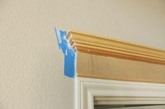 the corner of a wall with blue tape on it and a window frame in front of it