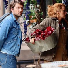 a man and woman walking down the street with flowers in their buckets on their backs