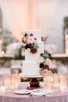 a white wedding cake sitting on top of a table next to some glasses and candles