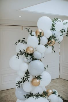 white and gold balloons with greenery on them in the shape of a tower for a wedding reception