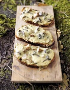 three slices of bread with cheese and mushrooms on them sitting on a wooden cutting board