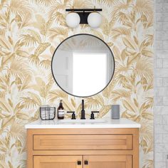 a bathroom vanity with a round mirror above it and palm leaves on the wall behind it