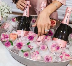 a woman holding three bottles of champagne in front of some ice cubes and flowers