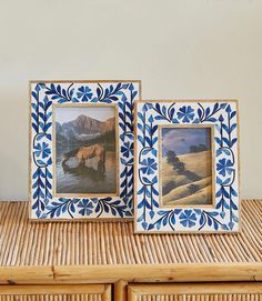 two framed pictures sitting next to each other on a wooden table with wicker drawers