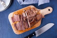 sliced meat sitting on top of a cutting board next to a knife and plate with utensils