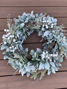 a wreath with pine cones and greenery is sitting on a wooden decking area