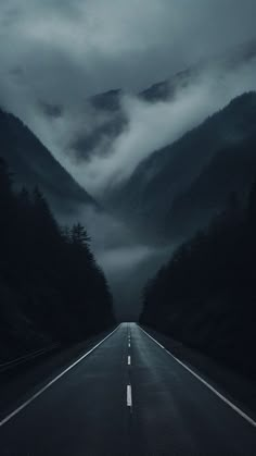 an empty road with mountains in the background and foggy skies above it at night