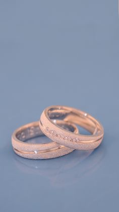 two gold wedding bands with diamonds on them, sitting side by side against a blue background