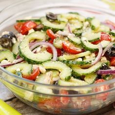 a glass bowl filled with cucumbers, onions and olives on top of a cutting board